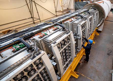 A Microsoft Project Natick technician in a blue hard hat works on a rack of computer disks that is poised to be inserted into a large tube.