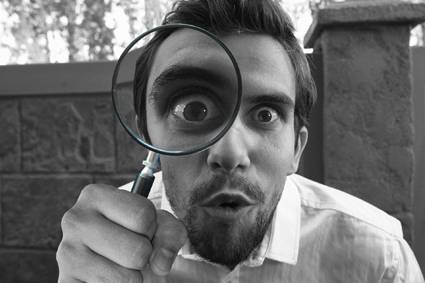 Goofy black and white photo of man with goatee holding up a magnifying glass. The eye behind the glass is exaggerated for comic effect.